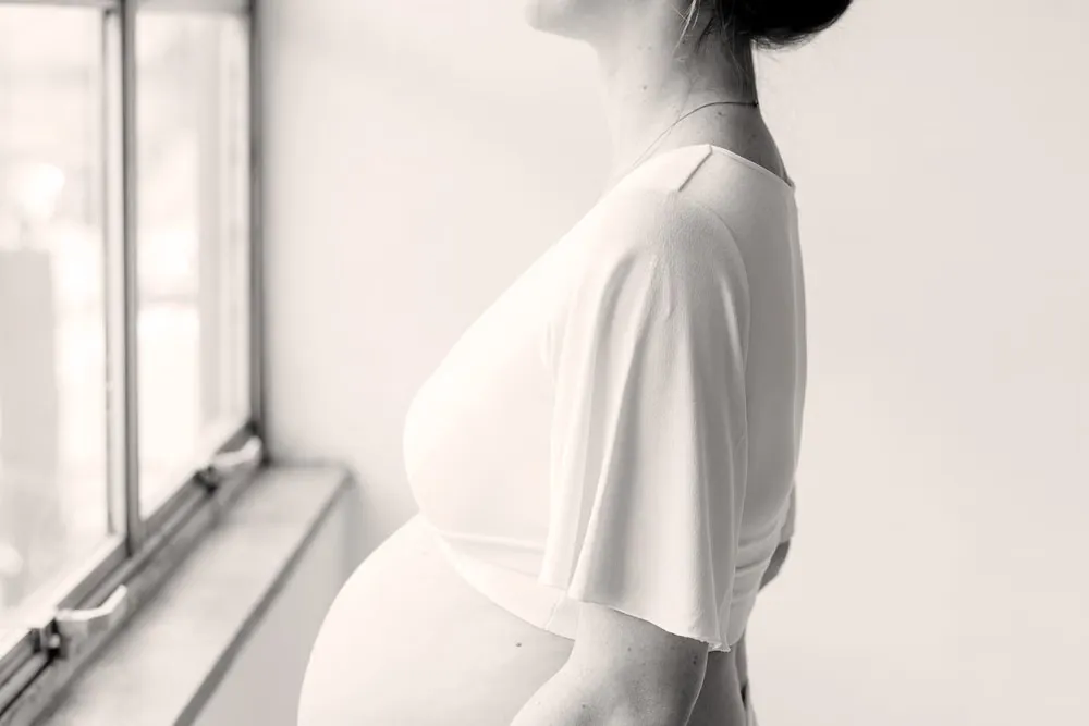 柔らかな光の差す窓辺に立つ妊娠中の女性