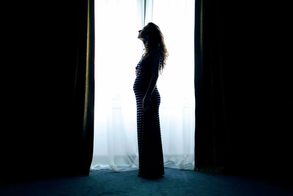 明るい窓辺に立つ妊婦のシルエット