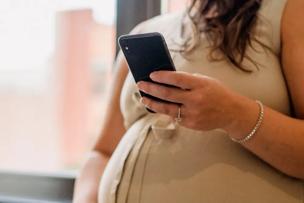 窓辺でスマートフォンを見る妊娠中の女性