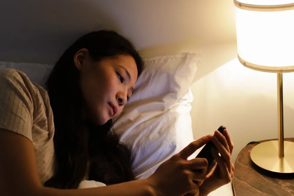夜のベッドでスマートフォンを見る女性