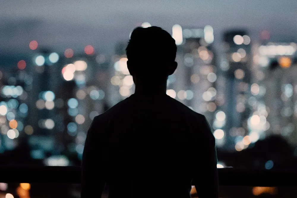 夜の街明かりを背にベランダに立つ男性のシルエット